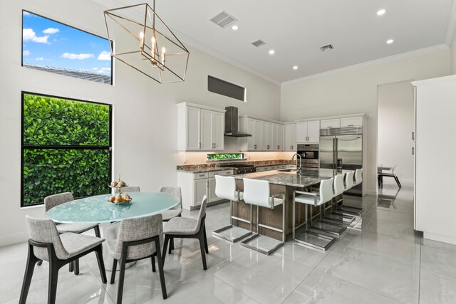 kitchen with a kitchen island with sink, dark stone counters, white cabinets, sink, and wall chimney exhaust hood