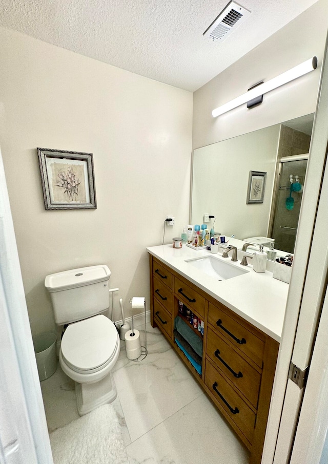 bathroom with vanity, a textured ceiling, toilet, and a shower with shower door