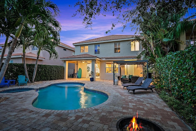 pool at dusk with a patio, an outdoor living space with a fire pit, and ceiling fan