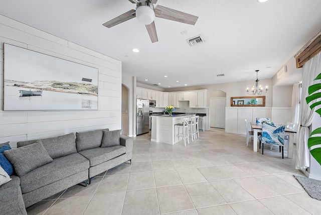 tiled living room featuring ceiling fan with notable chandelier