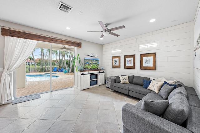 living room with ceiling fan, wood walls, a textured ceiling, and light tile patterned floors