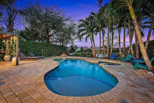 pool at dusk with an in ground hot tub, pool water feature, and a patio area