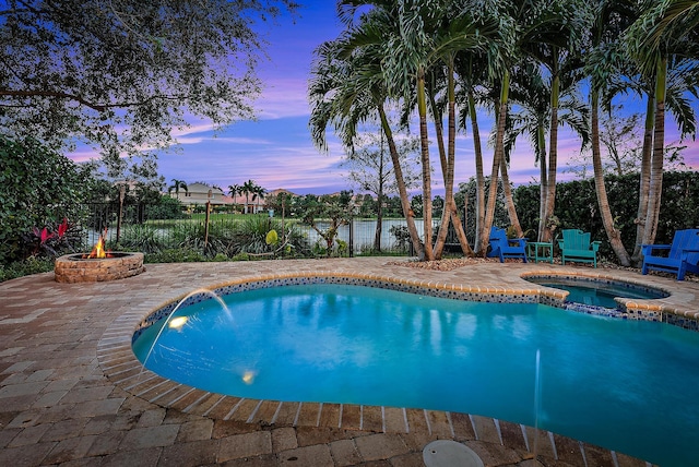 pool at dusk featuring an in ground hot tub, a water view, an outdoor fire pit, and a patio