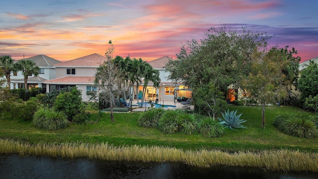 back house at dusk featuring a water view, a patio area, and a lawn