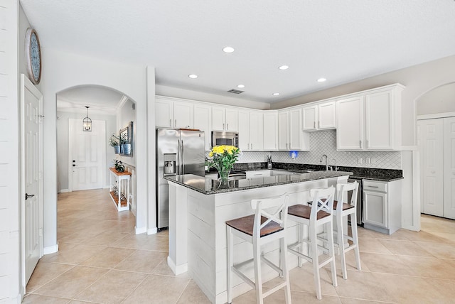 kitchen featuring appliances with stainless steel finishes, dark stone countertops, a center island, white cabinets, and decorative backsplash