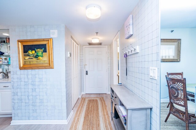 corridor with light wood-type flooring and tile walls