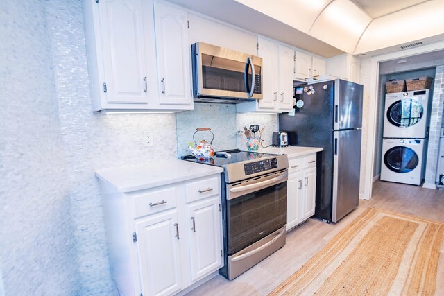 kitchen with appliances with stainless steel finishes, backsplash, light hardwood / wood-style flooring, stacked washer and clothes dryer, and white cabinets