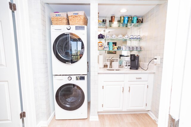 laundry area with stacked washing maching and dryer, sink, and light hardwood / wood-style flooring