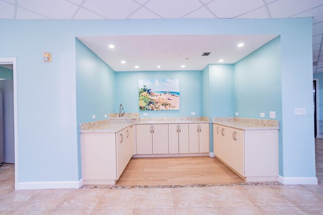 kitchen featuring a drop ceiling, sink, light tile patterned floors, light stone counters, and kitchen peninsula