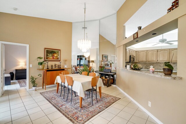 dining space with a towering ceiling, ceiling fan with notable chandelier, and light tile patterned floors