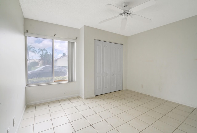 unfurnished bedroom with ceiling fan, light tile patterned floors, a closet, and a textured ceiling