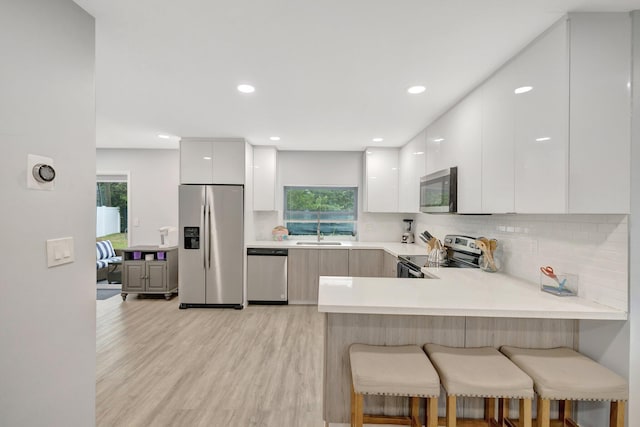 kitchen with kitchen peninsula, appliances with stainless steel finishes, a breakfast bar, white cabinets, and light wood-type flooring