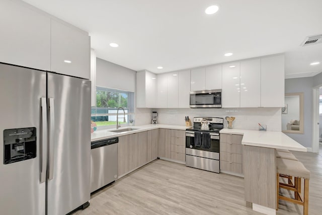 kitchen with sink, stainless steel appliances, kitchen peninsula, a breakfast bar, and white cabinets