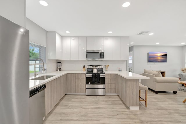 kitchen with sink, stainless steel appliances, kitchen peninsula, light hardwood / wood-style floors, and a kitchen bar