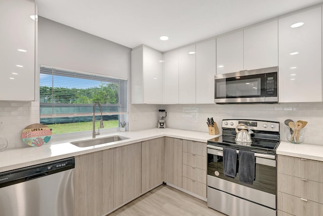 kitchen featuring appliances with stainless steel finishes, tasteful backsplash, sink, light hardwood / wood-style flooring, and white cabinets