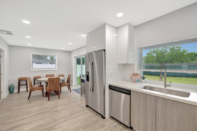 kitchen with light wood-type flooring, stainless steel appliances, white cabinetry, and sink