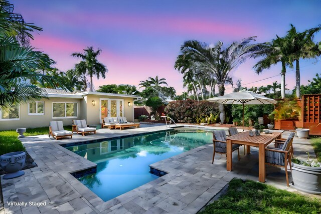 pool at dusk featuring french doors and a patio