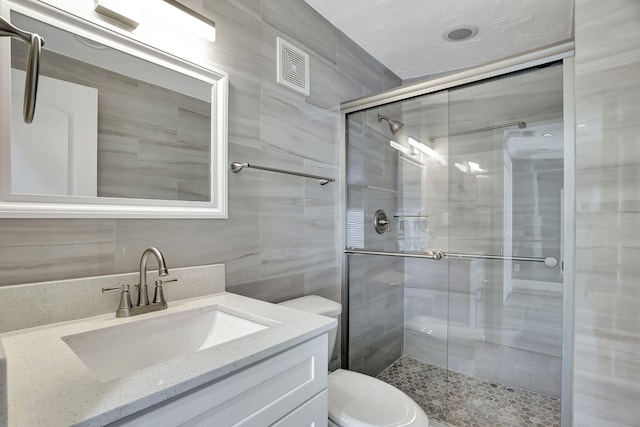 bathroom with a shower with shower door, tile walls, toilet, and vanity