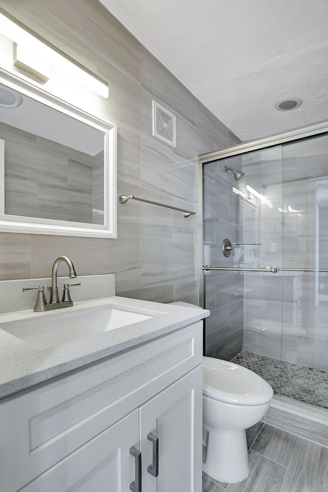 bathroom featuring toilet, tile walls, a shower with shower door, and vanity