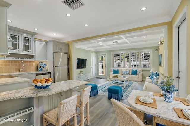 kitchen with light hardwood / wood-style floors, decorative backsplash, coffered ceiling, gray cabinetry, and stainless steel appliances