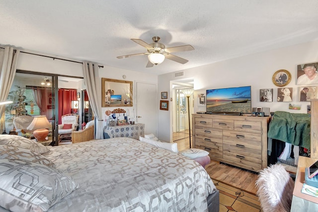 bedroom with ceiling fan, ensuite bath, a textured ceiling, and light hardwood / wood-style flooring