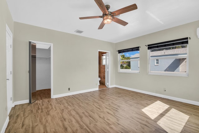 unfurnished bedroom with a walk in closet, ensuite bath, ceiling fan, light hardwood / wood-style floors, and a closet