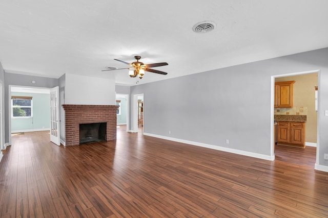 unfurnished living room with visible vents, dark wood-type flooring, a ceiling fan, a brick fireplace, and baseboards