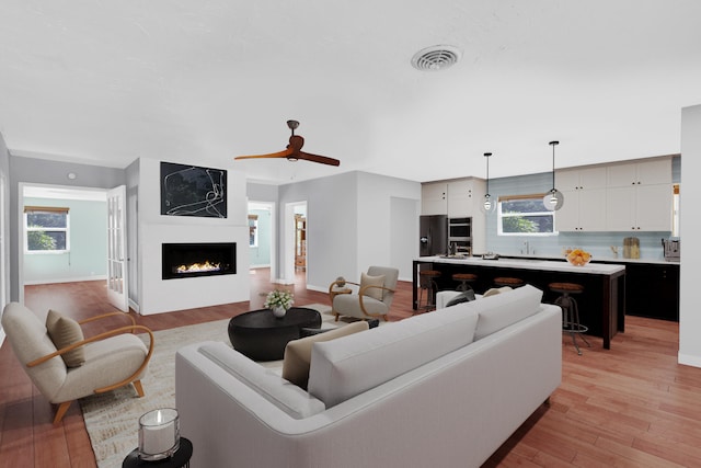 living room featuring light wood-style flooring, a fireplace, visible vents, and baseboards