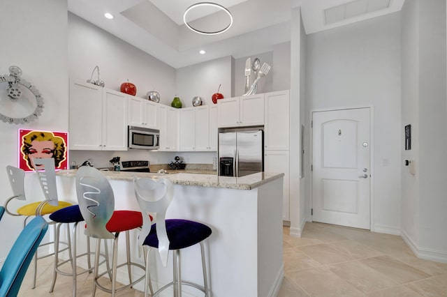 kitchen with white cabinets, light stone counters, a towering ceiling, and appliances with stainless steel finishes