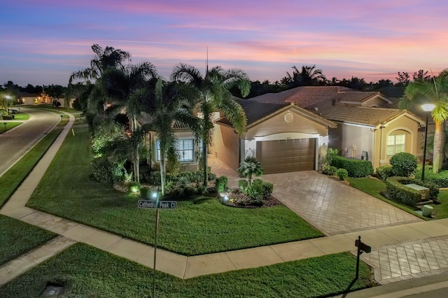 mediterranean / spanish home with a garage, a front lawn, decorative driveway, and stucco siding