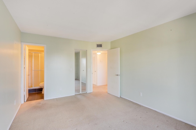 unfurnished bedroom with light colored carpet, ensuite bathroom, and a closet