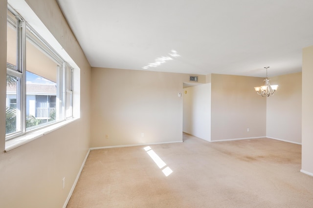 empty room with light carpet and a notable chandelier