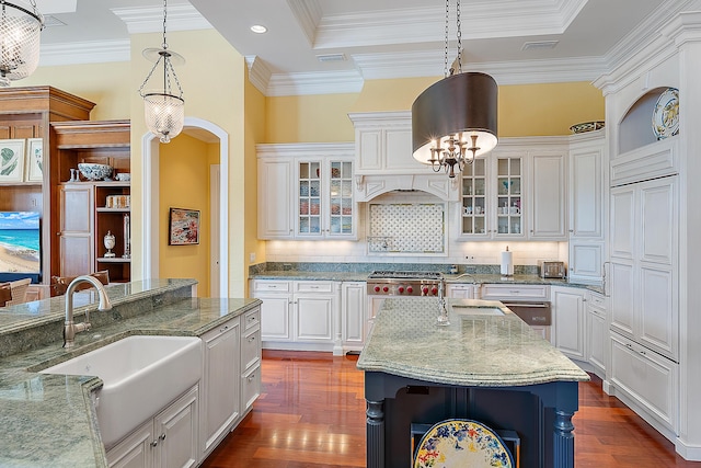 kitchen with backsplash, dark stone counters, sink, an island with sink, and decorative light fixtures