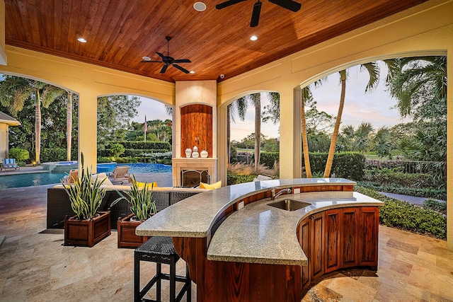 patio terrace at dusk with exterior fireplace, ceiling fan, and a wet bar