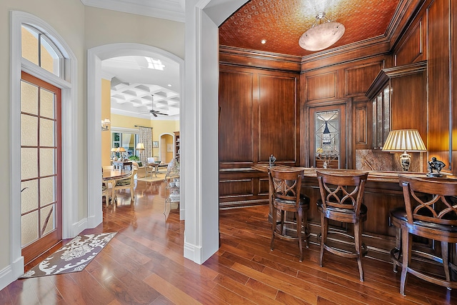 bar with crown molding, ceiling fan, dark wood-type flooring, and coffered ceiling