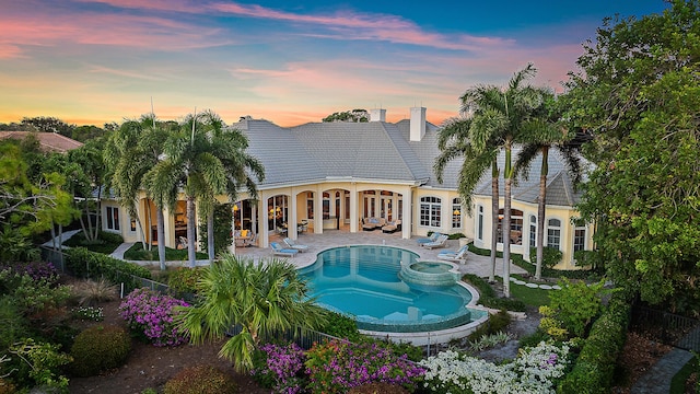 pool at dusk featuring outdoor lounge area, an in ground hot tub, and a patio