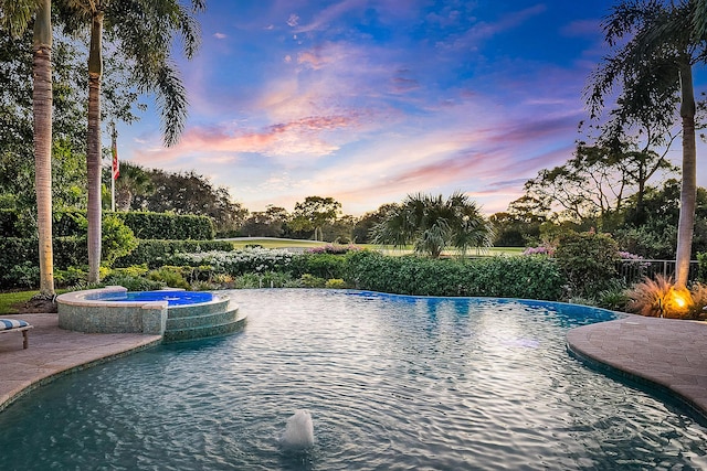 pool at dusk featuring an in ground hot tub and pool water feature