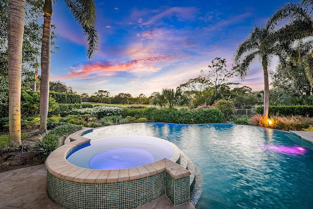 pool at dusk featuring an in ground hot tub