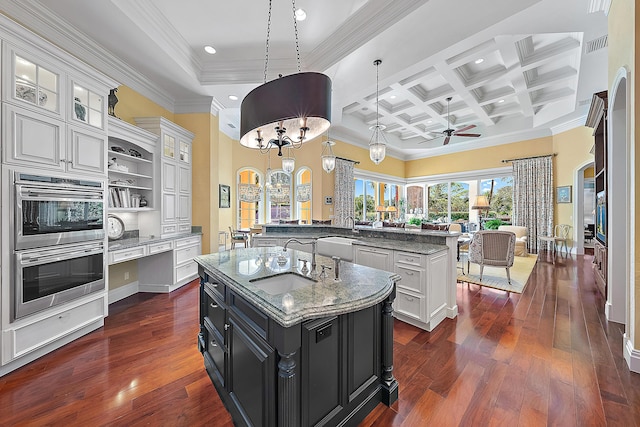 kitchen featuring white cabinets, ceiling fan with notable chandelier, ornamental molding, an island with sink, and decorative light fixtures