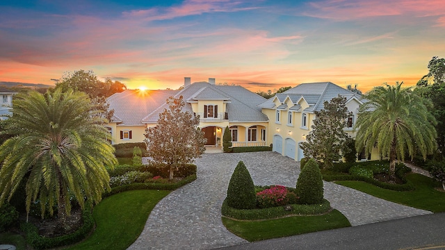 french country home with covered porch, a balcony, a garage, and a lawn