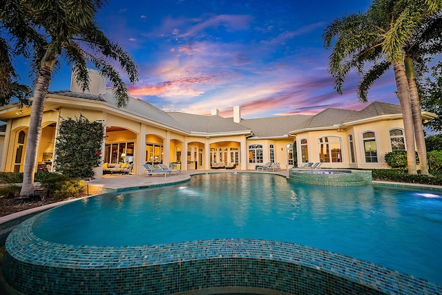 pool at dusk with an in ground hot tub and a patio