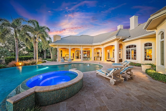 pool at dusk featuring an in ground hot tub and a patio