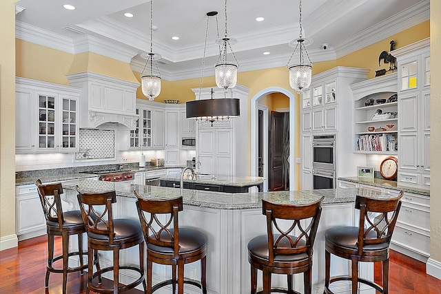 kitchen with dark hardwood / wood-style flooring, a tray ceiling, pendant lighting, a spacious island, and a kitchen bar