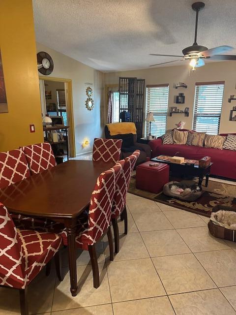 tiled dining area with ceiling fan, vaulted ceiling, and a textured ceiling