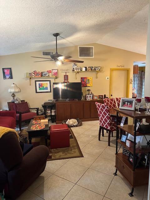 living room with ceiling fan, vaulted ceiling, a textured ceiling, and light tile patterned floors