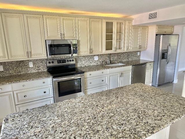 kitchen with light stone countertops, decorative backsplash, stainless steel appliances, sink, and cream cabinets