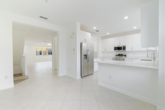 kitchen with sink, kitchen peninsula, light tile patterned floors, appliances with stainless steel finishes, and white cabinetry