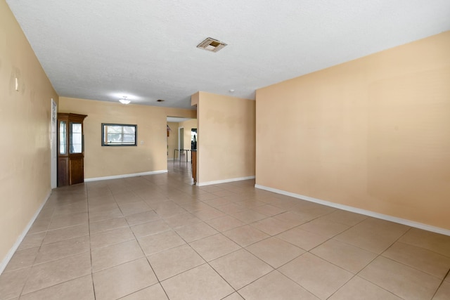 empty room with light tile patterned floors, baseboards, visible vents, and a textured ceiling