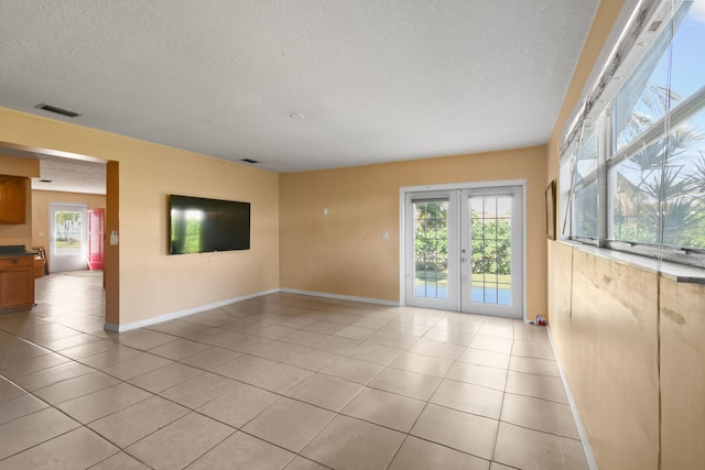 empty room with light tile patterned floors, a textured ceiling, visible vents, baseboards, and french doors