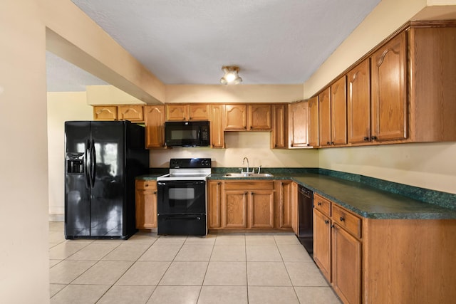 kitchen featuring brown cabinets, light tile patterned floors, dark countertops, a sink, and black appliances